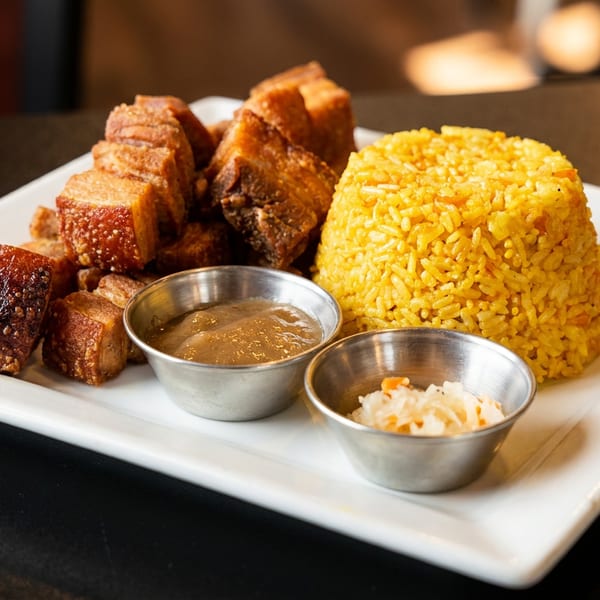 Crispy pork belly, yellow rice, and two dipping sauces served on a white rectangular plate.