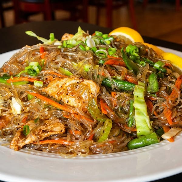 Glass noodles with chicken, carrots, green beans, and scallions, garnished with a lemon wedge.