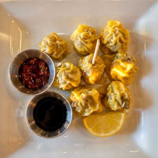 Nine golden dumplings on a white plate with two sauces and a lemon slice.