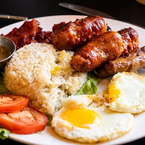 Filipino breakfast plate with garlic rice, longanisa, fried eggs, tomatoes, and lettuce.